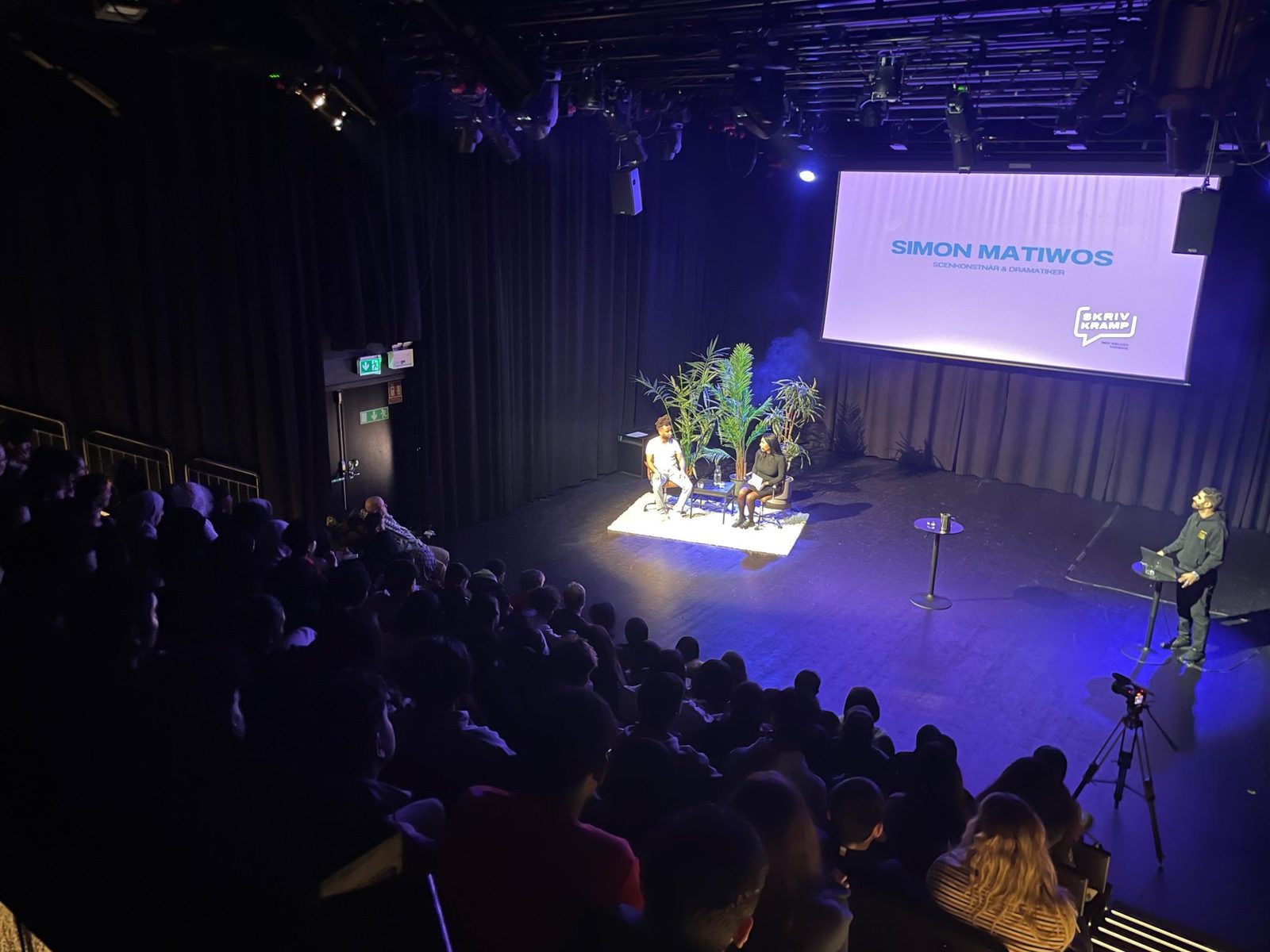 Fullsatt salong och Simon Matiwos namn på storbildsskärmen